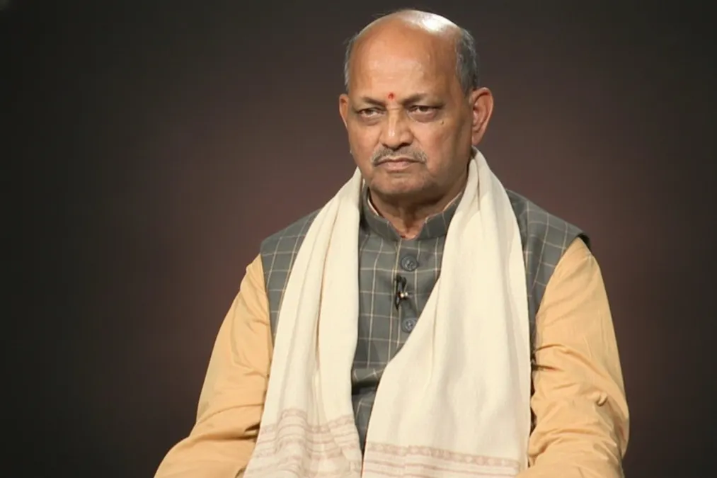 Manmohan Samal seated for a studio interview, wearing a checked waistcoat and a white shawl.
