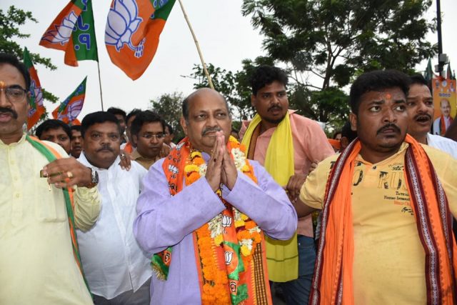 Manmohan Samal, garlanded and with hands folded in greeting, walking in a procession accompanied by party workers carrying flags.