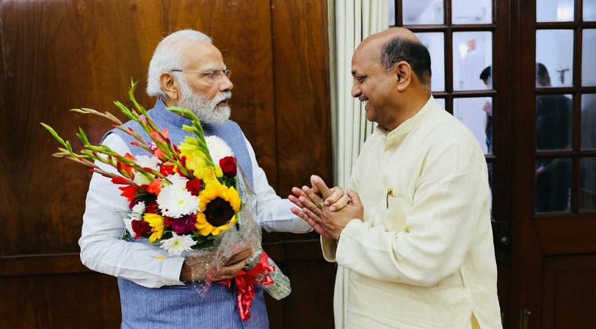 Manmohan Samal greeting Prime Minister Narendra Modi, who is holding a bouquet of flowers, at an indoor meeting.