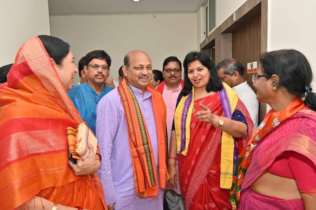Manmohan Samal in conversation with party colleagues, several of them women leaders wearing party scarves, at an indoor gathering.