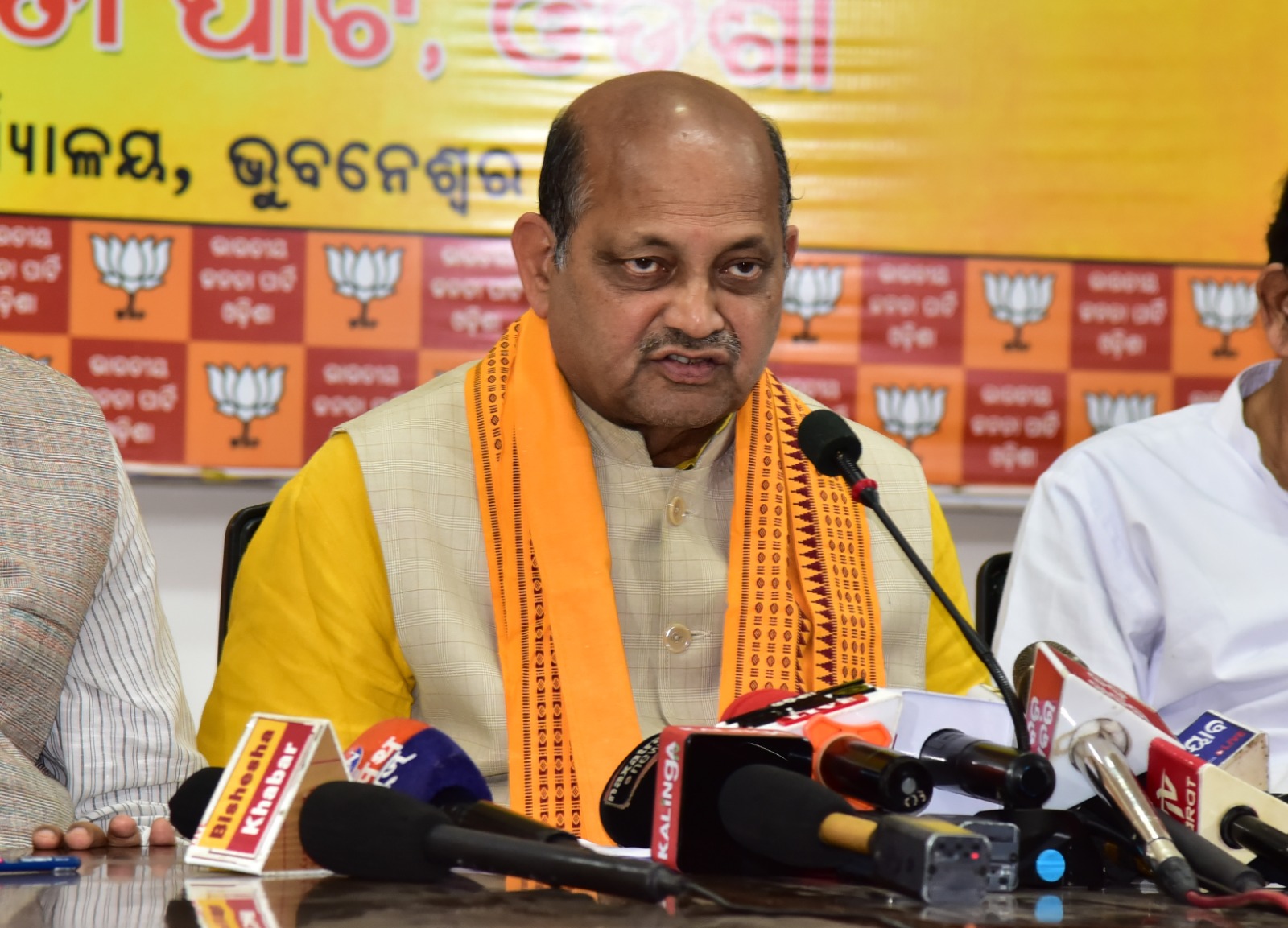 Manmohan Samal speaking at a press conference in Bhubaneswar, flanked by colleagues, before a backdrop of party emblems.