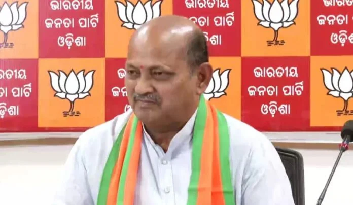 Manmohan Samal seated before a wall of Bharatiya Janata Party Odisha emblems at the state headquarters.