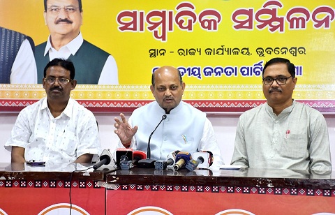 Manmohan Samal seated at a table between two colleagues during a press conference at the state party office.