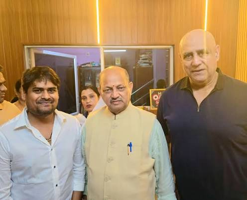 Manmohan Samal standing between two visitors for a photograph in an interior room.