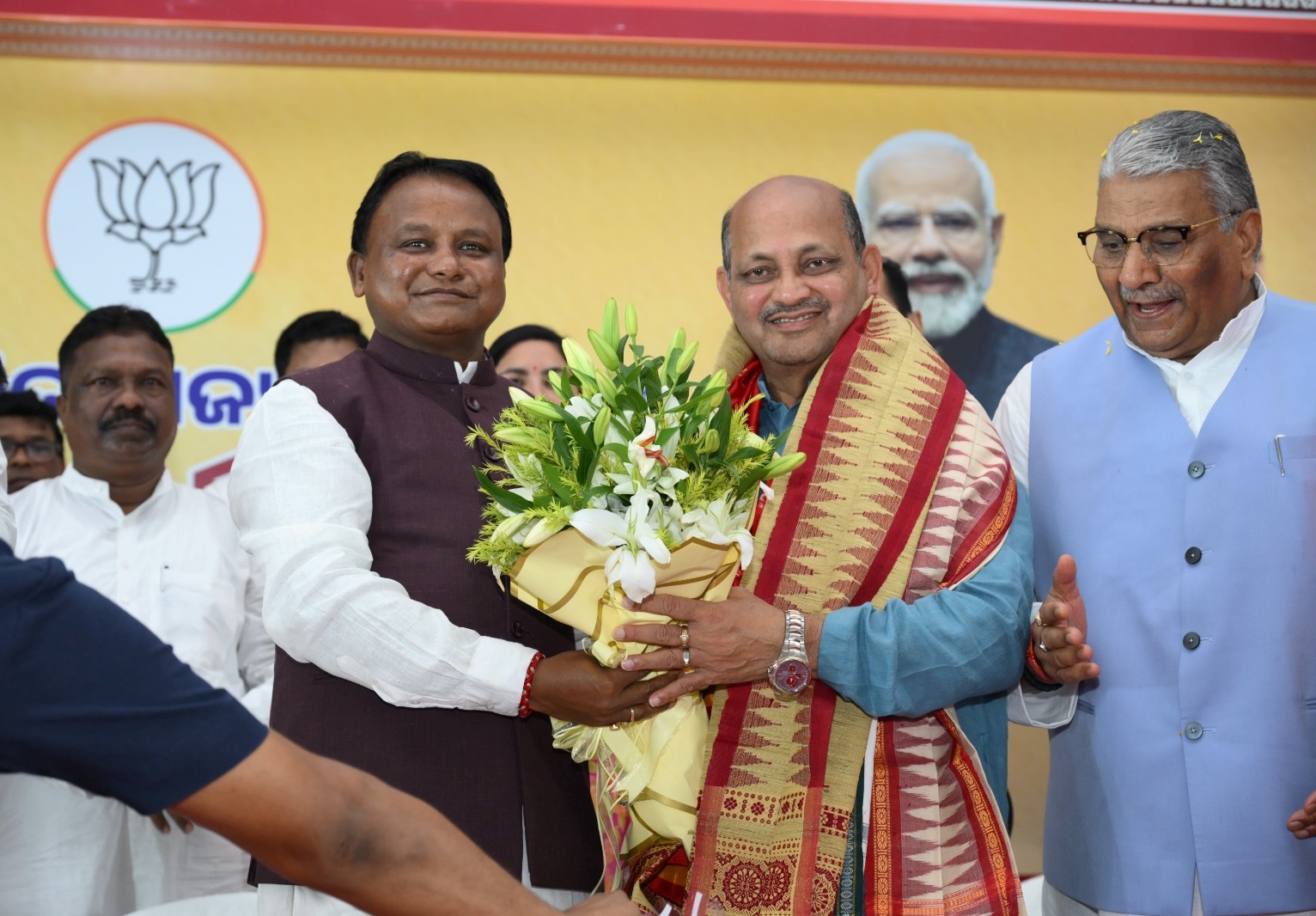 Manmohan Samal being presented with a bouquet by Chief Minister Mohan Charan Majhi on a stage bearing the party lotus emblem and a portrait of the Prime Minister.