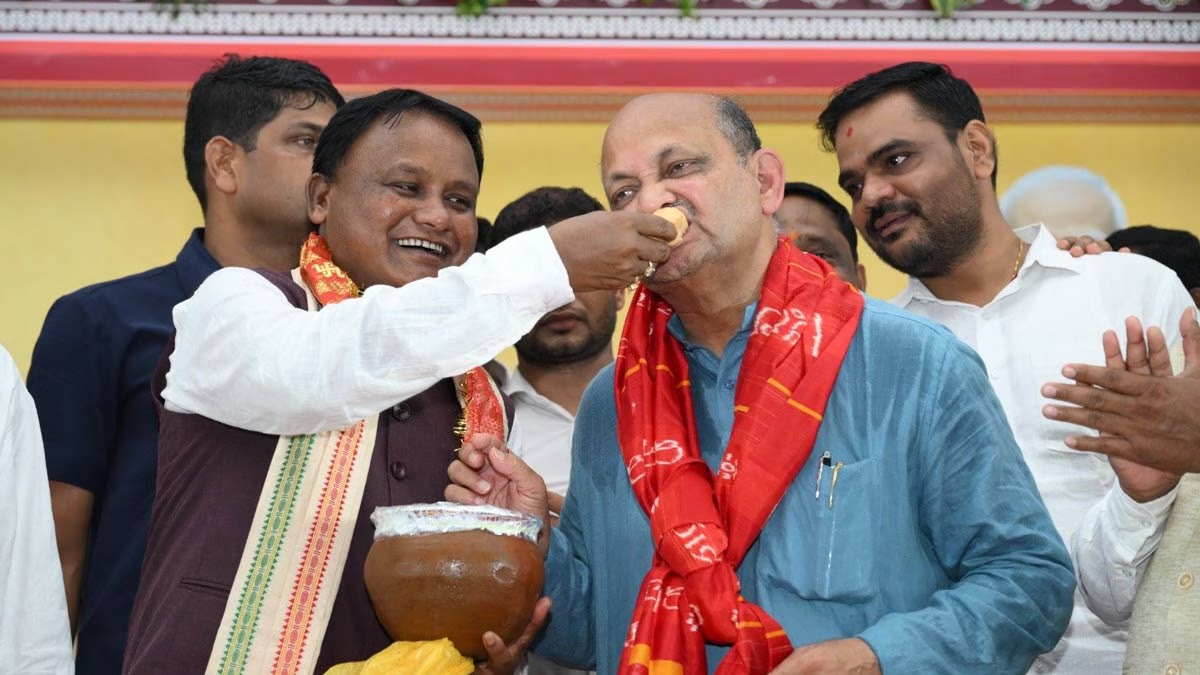 Chief Minister Mohan Charan Majhi offering sweets to Manmohan Samal at a celebration, surrounded by party workers.