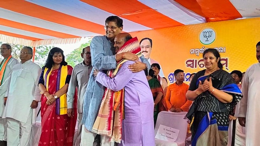 Manmohan Samal embracing Chief Minister Mohan Charan Majhi on a party stage while colleagues look on.